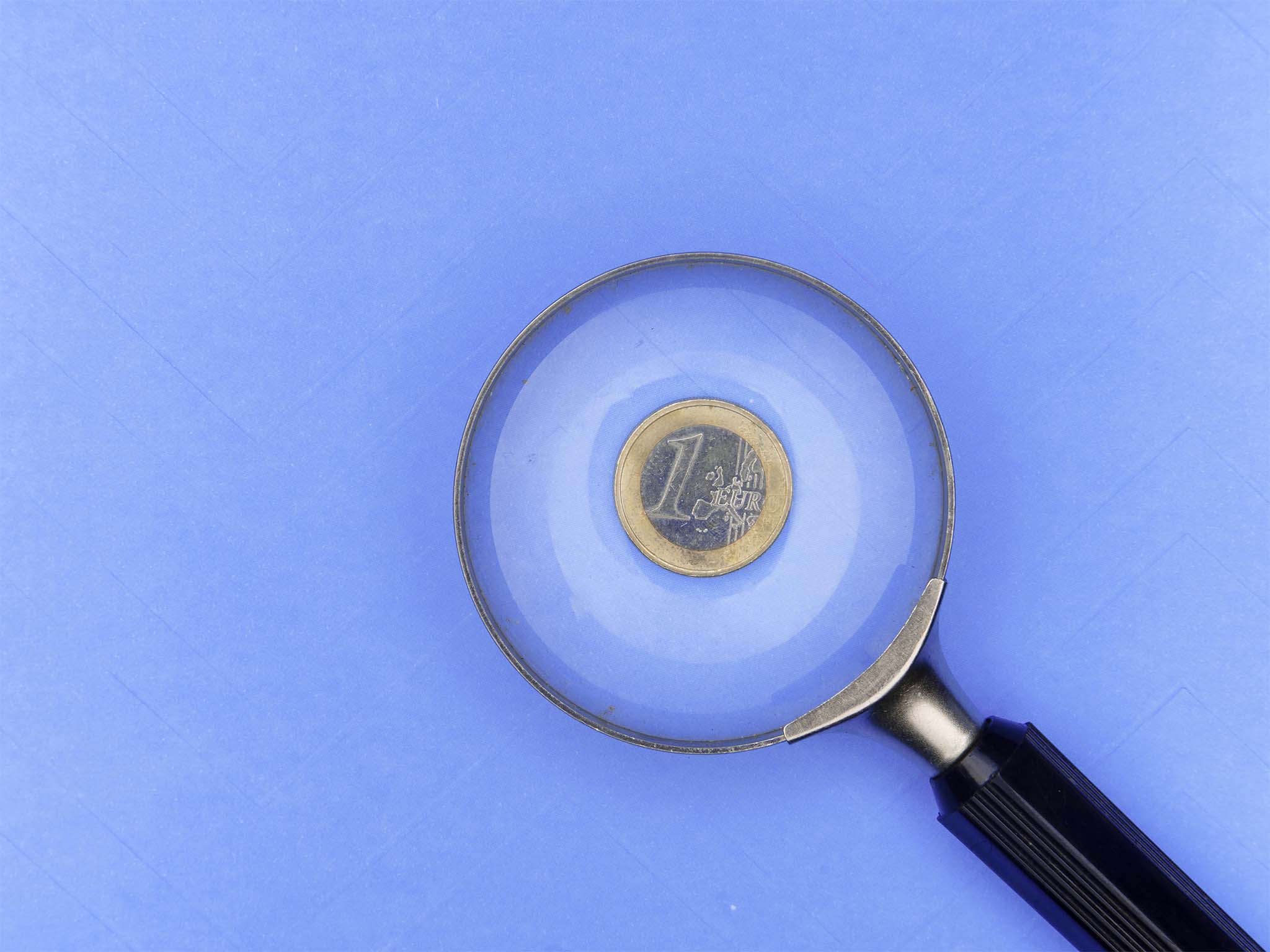 Magnifying glass over euro piece on blue background.
